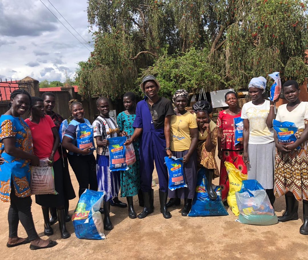 A SEW beneficiary and her agricultural trainer standing smiling in a lush green maize field on land rented for them by the SEW programme